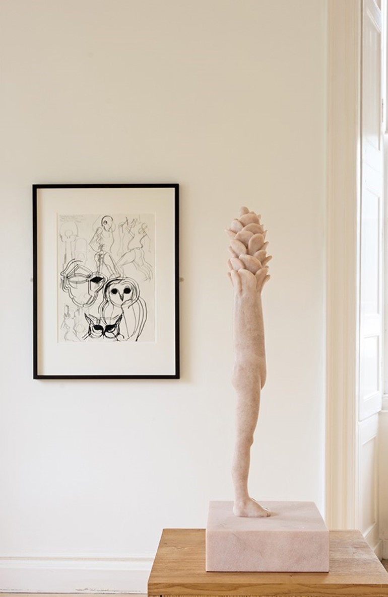 A black and white framed sketch drawing hangs on a wall with a marble scultpture in the foreground