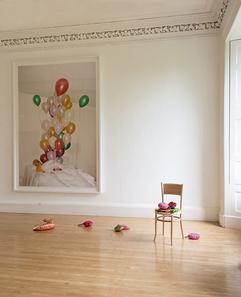 A large photograph of balloons hangs on a white wall with an empty chair in the foreground