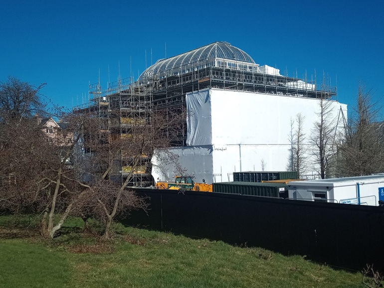 A glass house covered in scaffolding and partially wrapped in a white cover