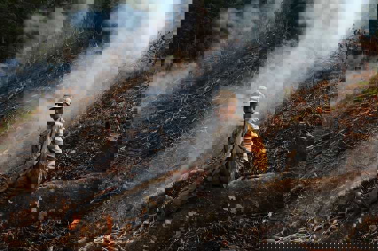 a young boy sits atop a tree trunk amidst smouldering vegetation