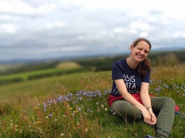 A smiling woman sitting on a hillside surrounded by flowers.