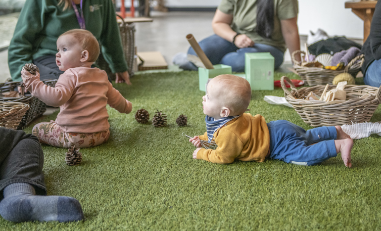 Babies playing on fake grass with natural objects.