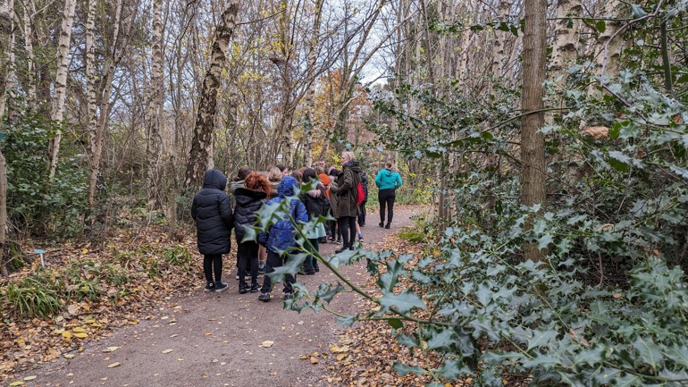A school class walking through Scottish woodland in the Garden.