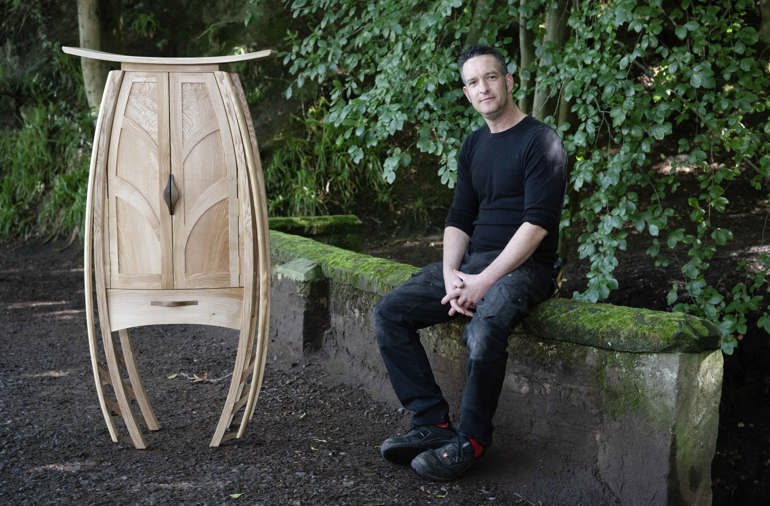 a man sits on a wall outside next to a wooden cabinet